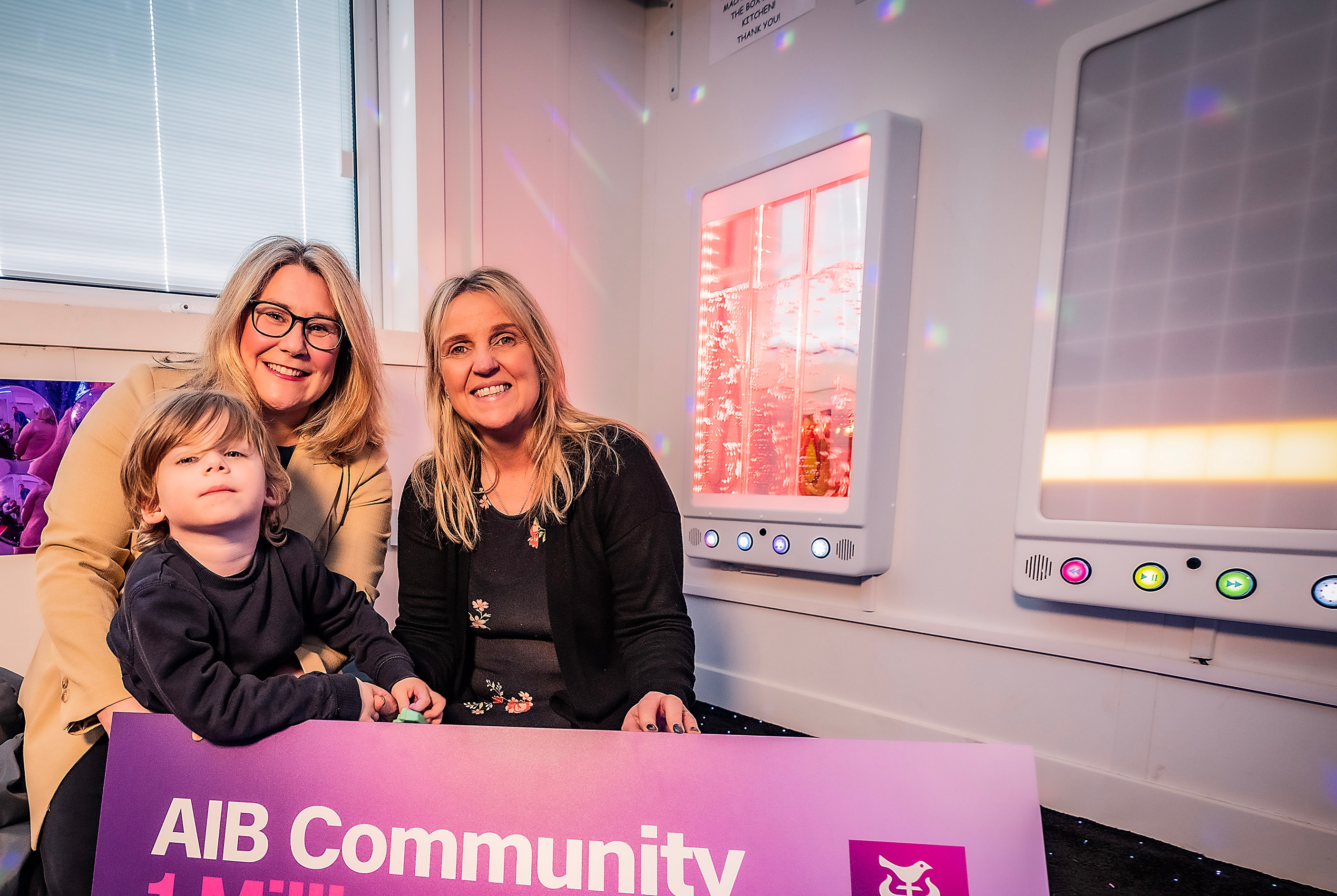 Two adults and a child in a sensory room with banner saying 2024 AIB Community €1 Million Fund Charities!