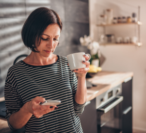A womon looking at her phone while drinking coffee